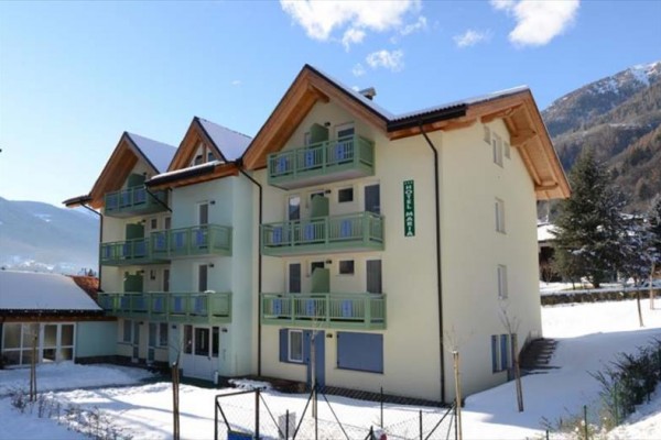 Budynek hotelu z balkonami na zaśnieżonym górskim tle.