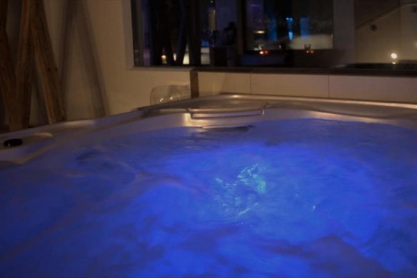 Niebiesko oświetlona wanna z hydromasażem w ciemnym pomieszczeniu.