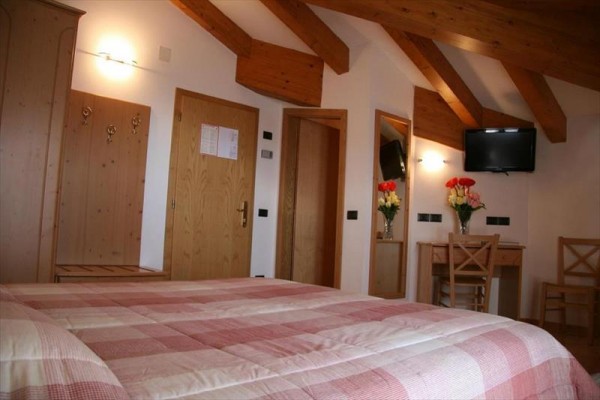 Pokój hotelowy z skośnym sufitem, łóżkiem, stołem i telewizorem na ścianie.