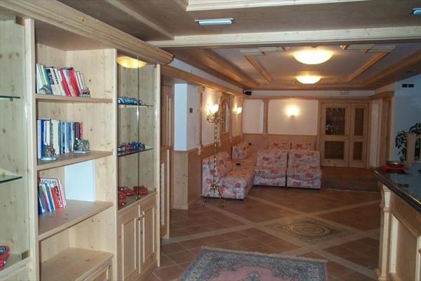 Salon z drewnianymi meblami, półkami z książkami i samochodzikami oraz kwiecistą sofą.