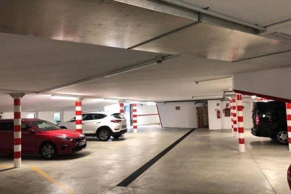 Podziemny parking z samochodami i słupami w czerwono-białe paski.