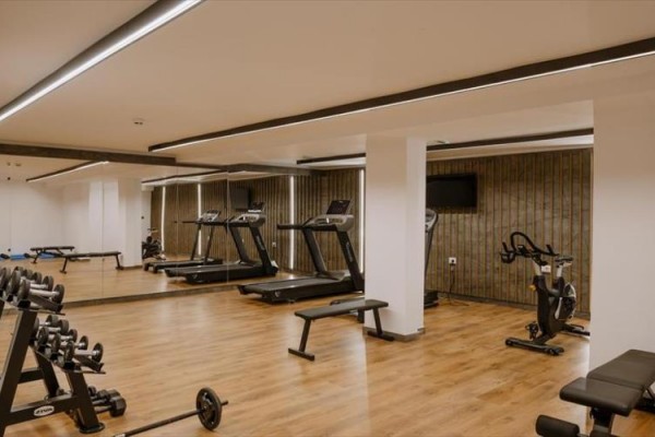 Centrum fitness z bieżniami, hantlami i rowerem stacjonarnym na drewnianej podłodze.