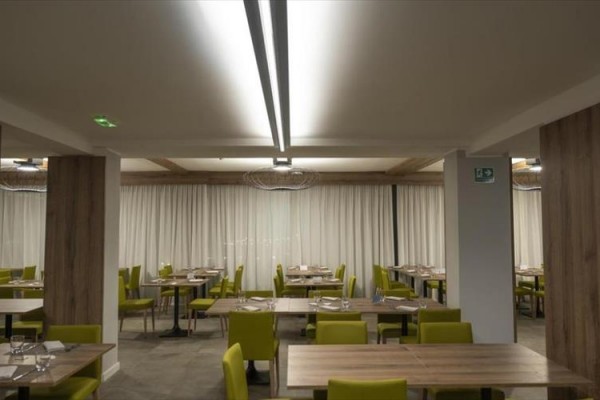 Restauracja z drewnianymi stołami i krzesłami z oliwkowo zielonymi siedziskami.