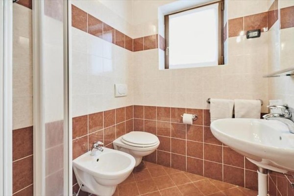 Łazienka z ceramiczną umywalką, bidetem, toaletą i małym oknem.
