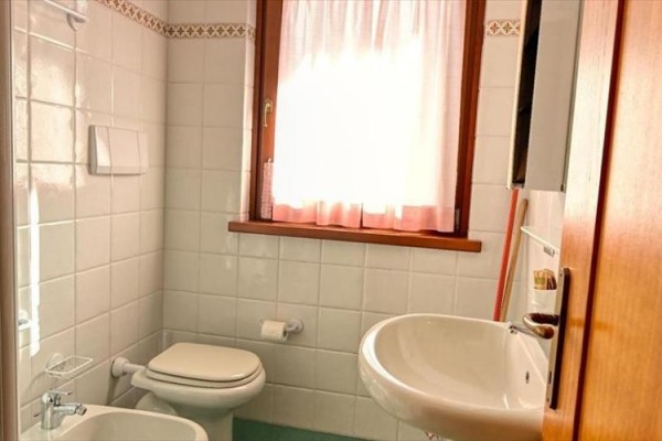 Łazienka z umywalką, toaletą i oknem z białymi zasłonami.