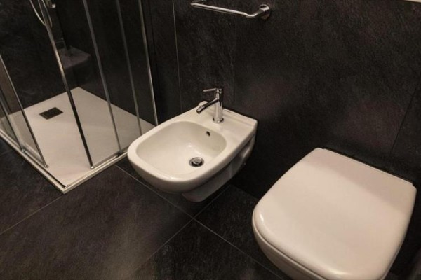 Jasny salon z szarą kanapą, wejściem do łazienki i szklanymi drzwiami na taras.  