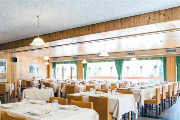 Restauracja z drewnianymi panelami, nakrytymi stołami i zasłonami przy oknach.